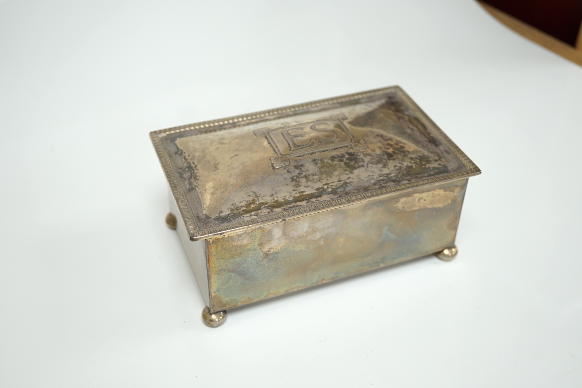 A George V Arts & Crafts silver mounted rectangular cigarette box, by Dryad Metal Works, Birmingham, 1924, on ball feet, the cover initialled ES, 15.2cm. Condition - fair